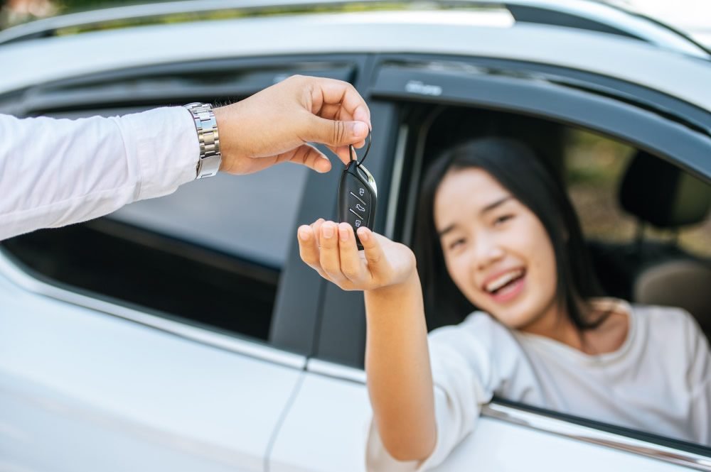 Wanita menerima kunci mobil dari sopir sebagai simbol proses rental mobil dengan sopir di Jakarta